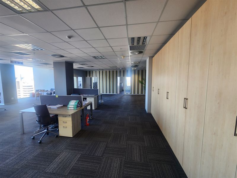 Spacious open-plan office area featuring suspended ceilings, recessed lighting, integrated air conditioning, and extensive built-in storage cabinetry with dark carpet flooring.