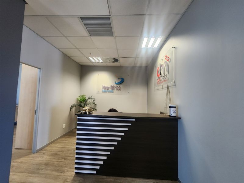 A professional office reception area featuring a modern built-in desk, suspended ceiling with recessed lighting, and durable laminate flooring.