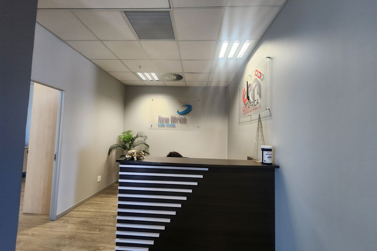 A professional office reception area featuring a modern built-in desk, suspended ceiling with recessed lighting, and durable laminate flooring.
