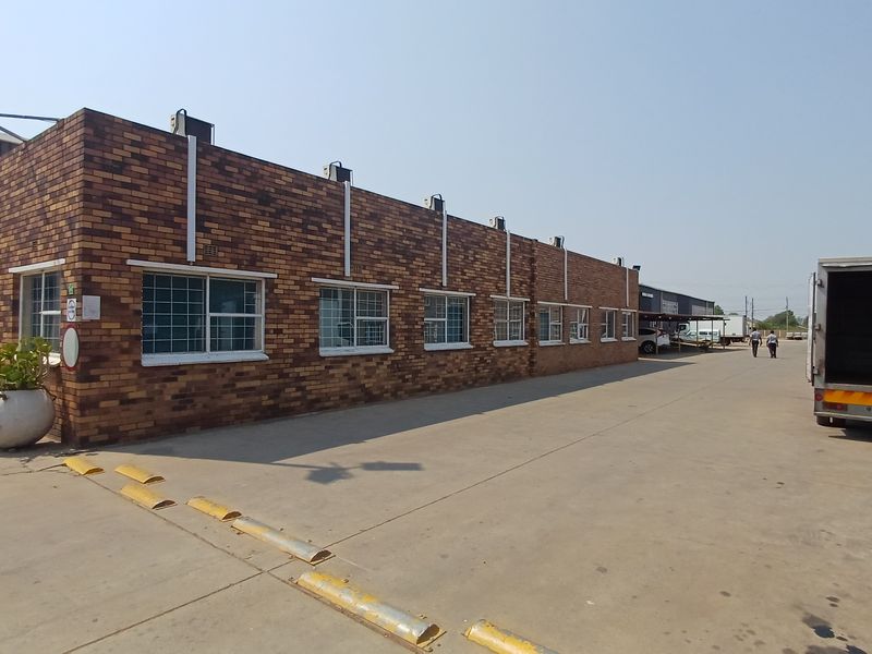 Exterior view of a commercial office building featuring a face-brick facade, security-barred windows, and a paved driveway with integrated speed bumps.