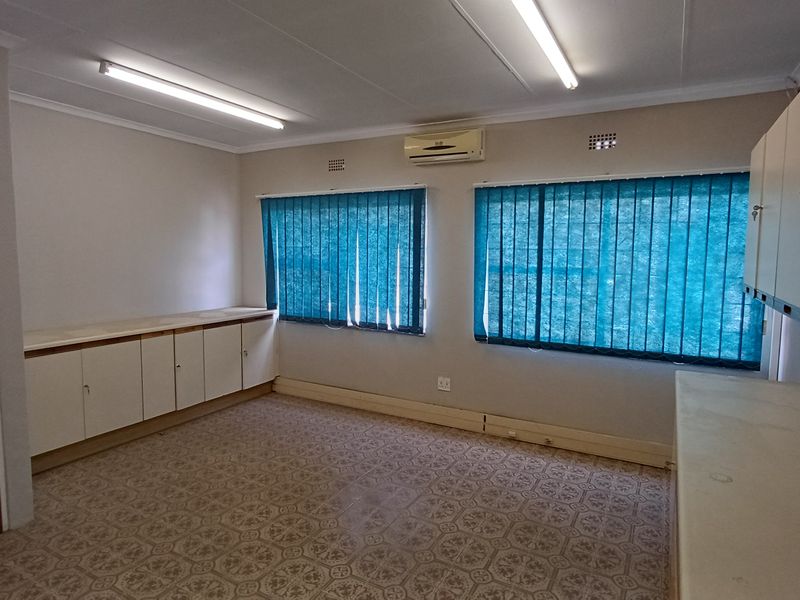 A functional office space featuring built-in storage cabinetry, split-system air conditioning, and large windows with vertical blinds.