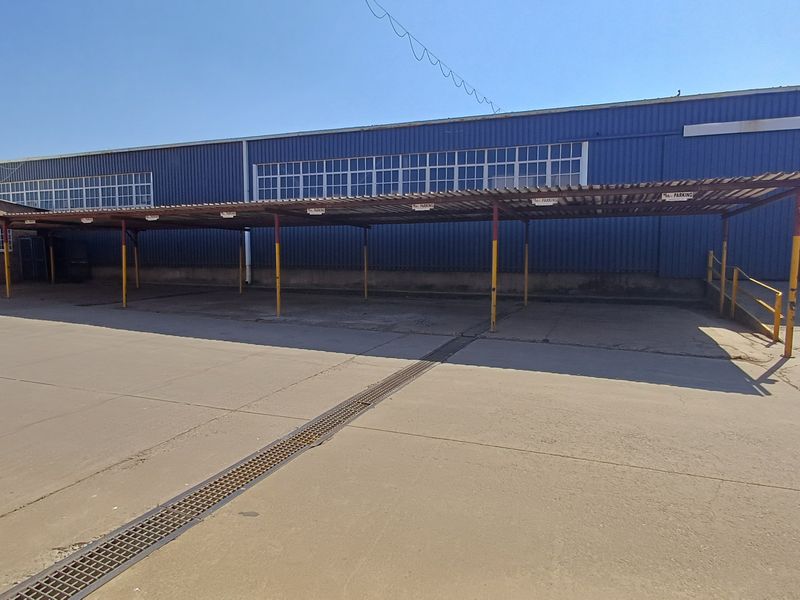 Rear exterior view of the office building featuring a large concrete parking area with a covered carport structure and steel access ramp.