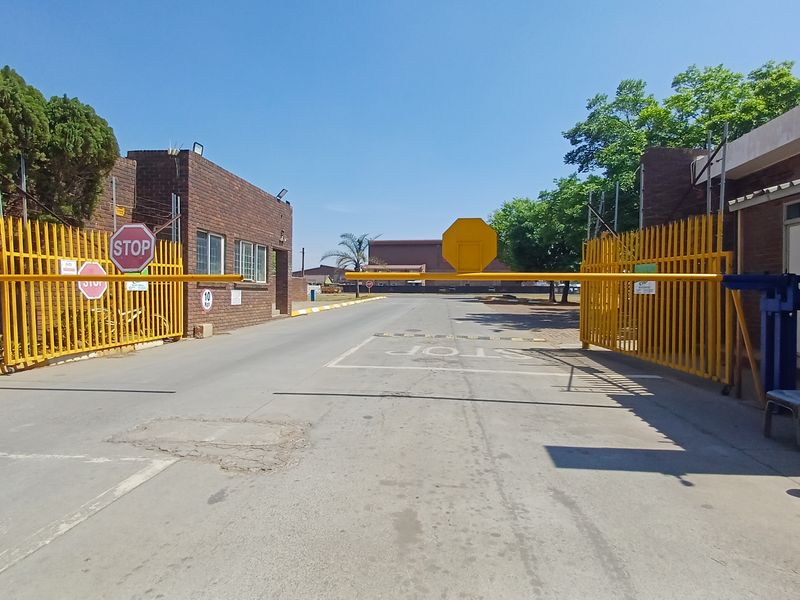 A secure office park entrance featuring a yellow boom gate, perimeter fencing, and brick building facades.