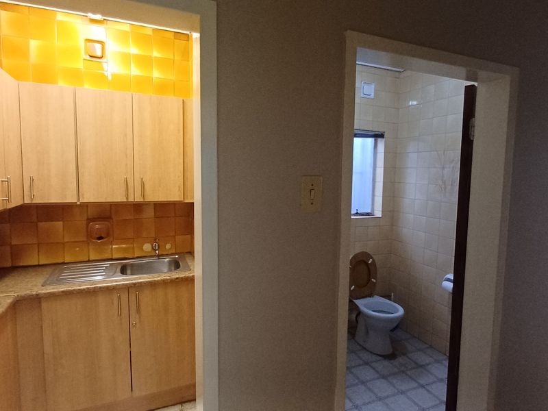 A view showing a small kitchenette with laminate cabinetry and a separate adjacent restroom with tiled finishes.