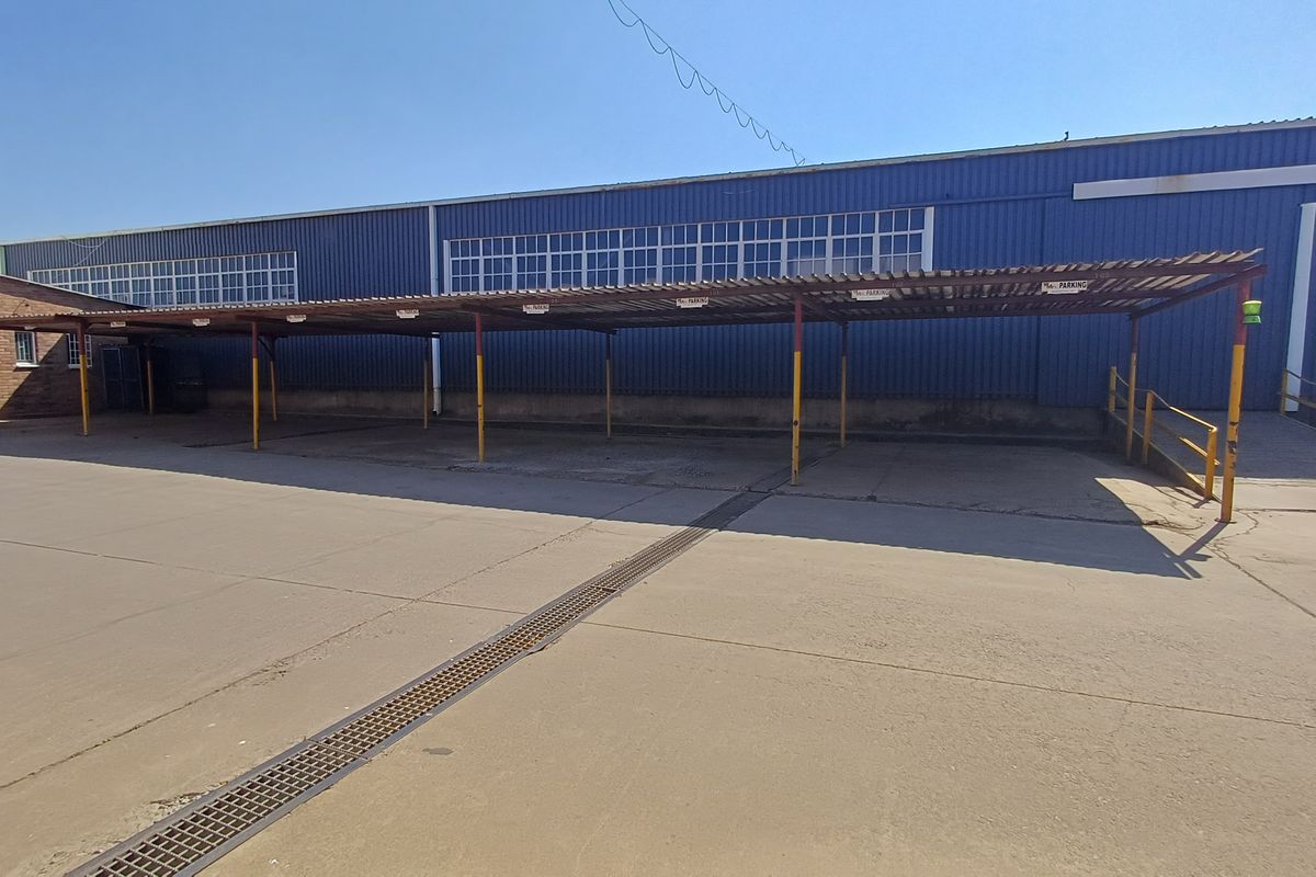 Rear exterior view of the office building featuring a large concrete parking area with a covered carport structure and steel access ramp.