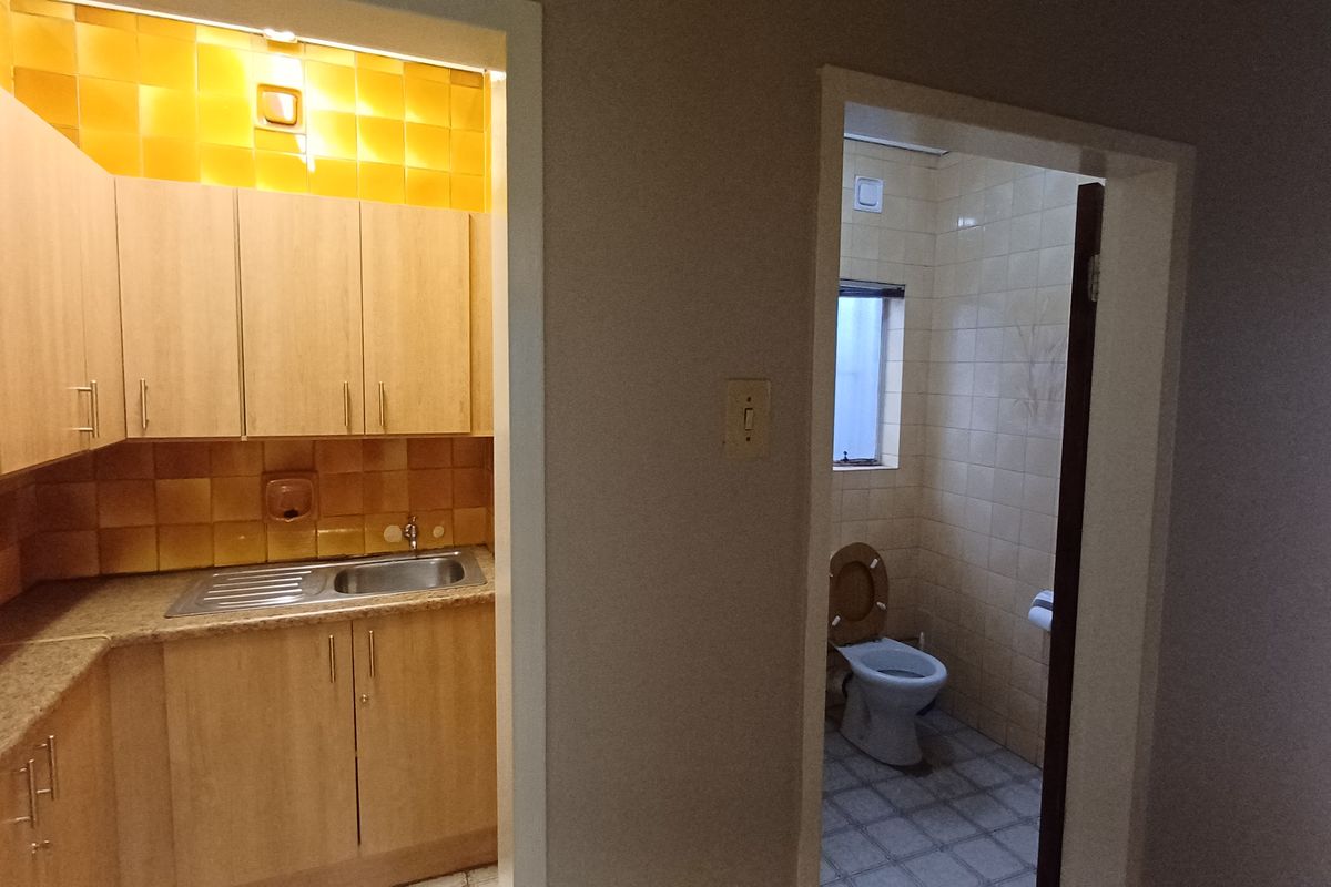 A view showing a small kitchenette with laminate cabinetry and a separate adjacent restroom with tiled finishes.