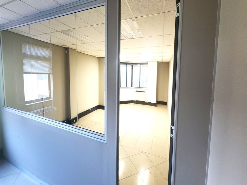 A vacant office space featuring a suspended ceiling, tiled flooring, and a glass partition wall, offering a clean and professional environment.