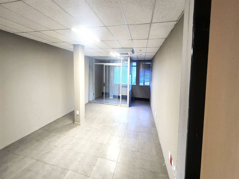 A clean, vacant office space featuring tiled flooring, a suspended ceiling, and a glass-partitioned meeting area with integrated air conditioning.