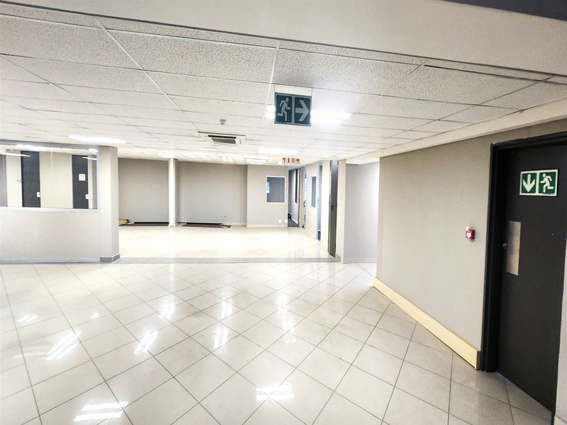 A spacious, open-plan office area featuring neutral wall finishes, ceramic tiled flooring, and a suspended ceiling with integrated lighting and air conditioning.