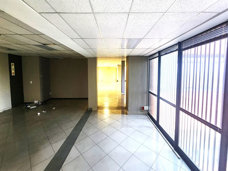 Spacious, vacant office area featuring large windows with vertical blinds, tiled flooring, and a suspended ceiling, offering a bright and open workspace.