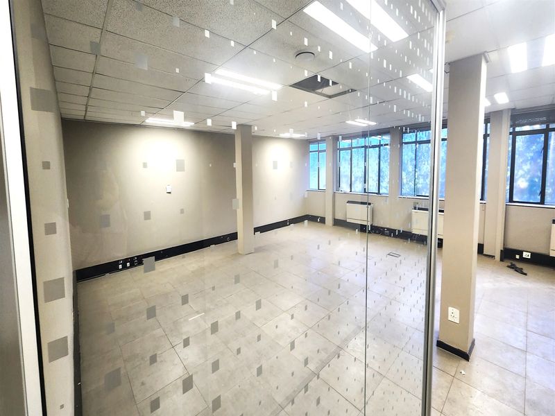 A bright, open-plan office space featuring a glass partition, suspended ceiling, tiled flooring, and integrated air conditioning units.