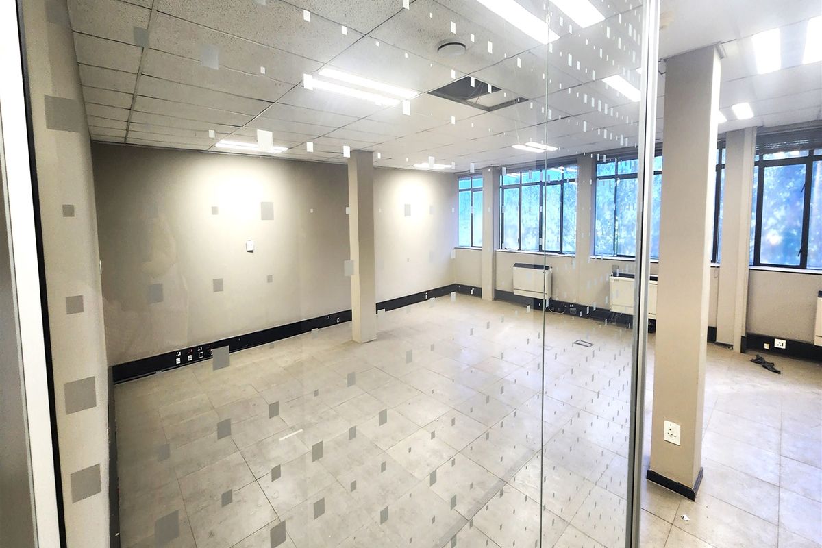 A bright, open-plan office space featuring a glass partition, suspended ceiling, tiled flooring, and integrated air conditioning units.