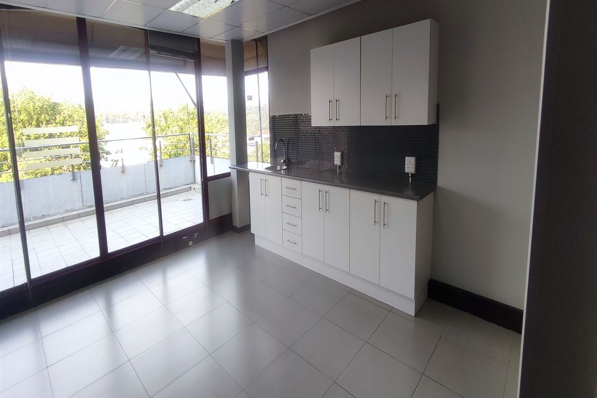 Office kitchenette featuring white cabinetry, stainless steel countertop, tiled backsplash, and direct access to a private balcony.