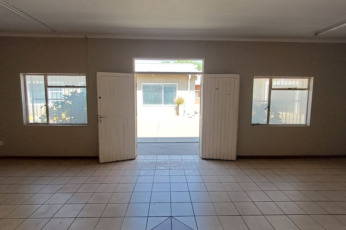 An empty, open-plan office space featuring tiled flooring, fluorescent lighting, and double doors leading to an exterior courtyard area.