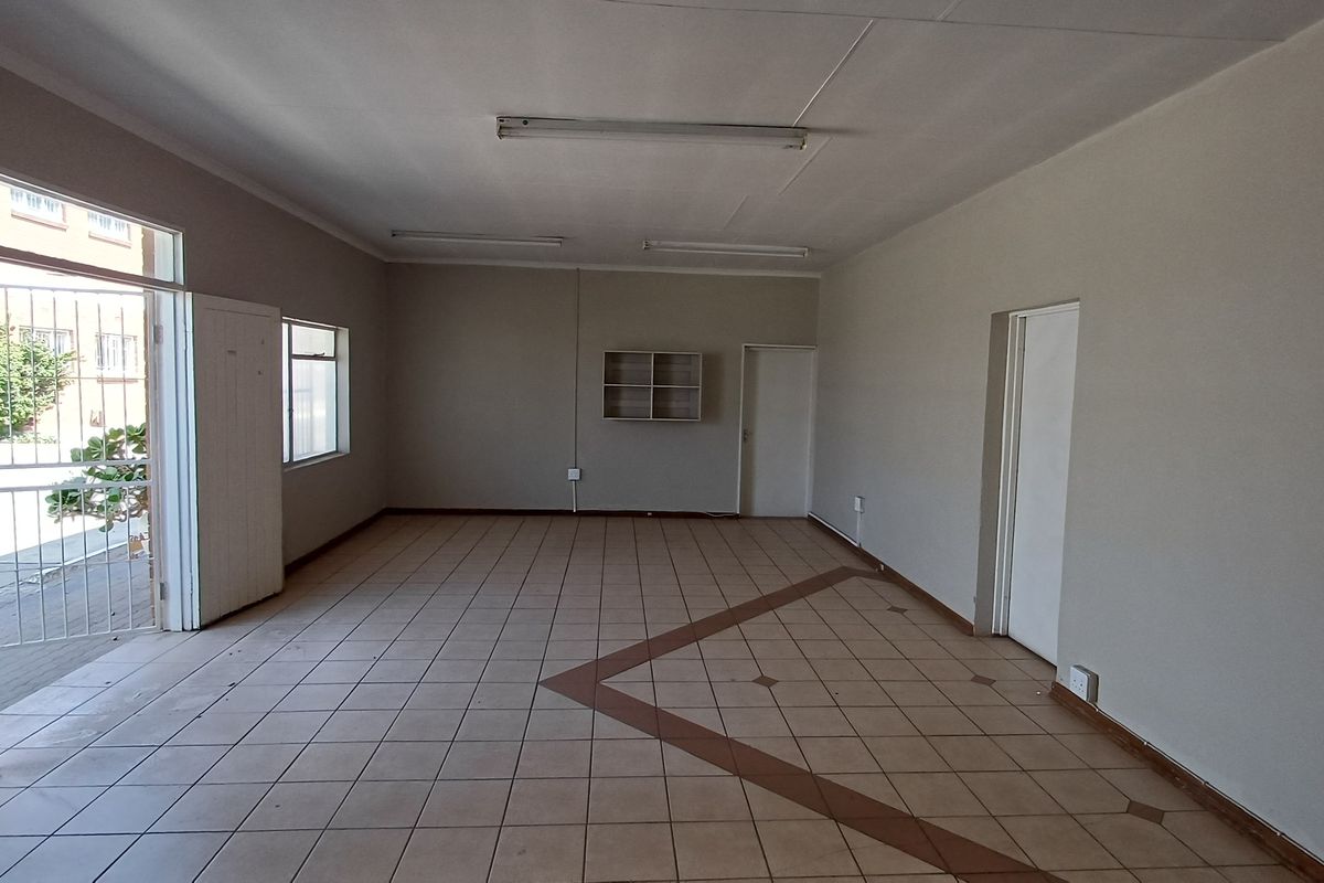 An empty, open-plan office space featuring tiled flooring, fluorescent lighting, and a secure entrance gate, suitable for a variety of professional business uses.