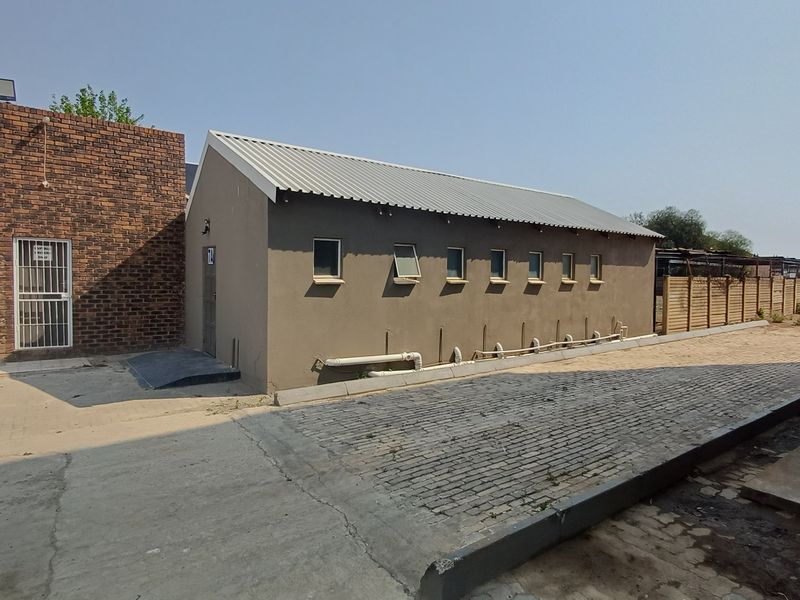 Exterior view of a commercial office building featuring a brick section, plastered walls, metal roofing, and paved access area.