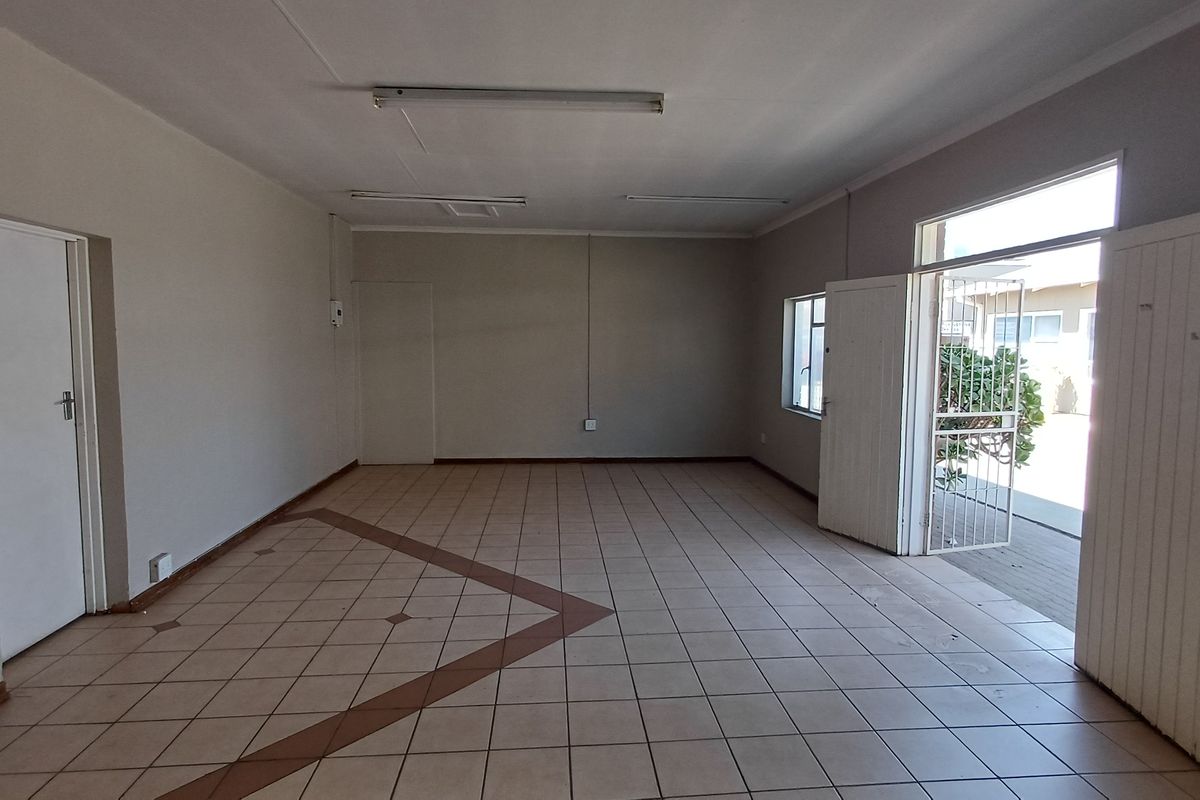 An empty, open-plan office space featuring ceramic tile flooring, fluorescent lighting, and direct access to an outdoor area via a security gate.
