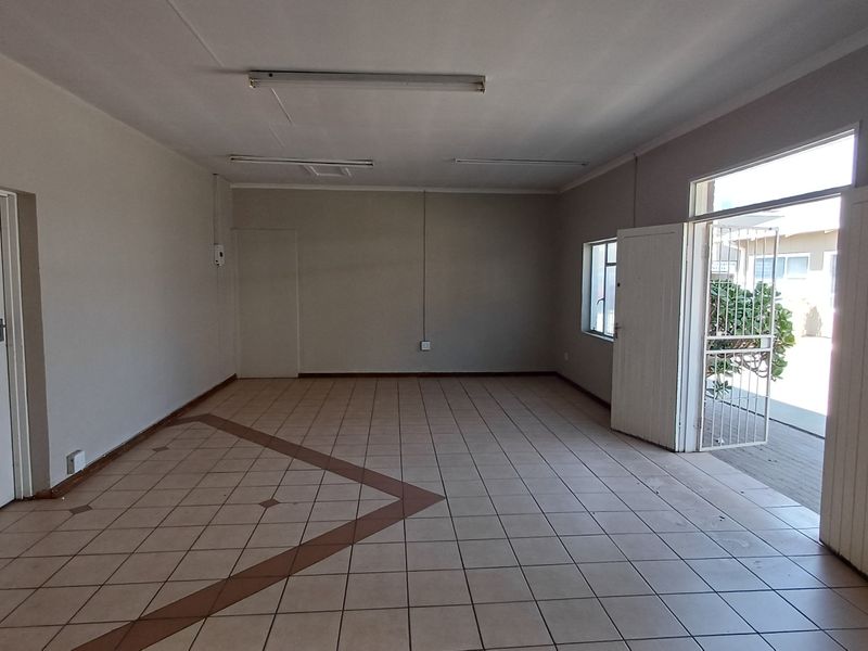 An empty, open-plan office space featuring ceramic tile flooring, fluorescent lighting, and direct access to an outdoor area via a security gate.
