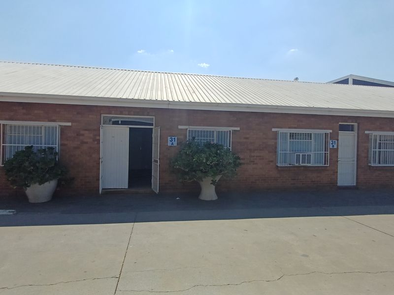Front exterior view of a single-story brick office building with metal roofing, security bars on windows, and a concrete driveway.