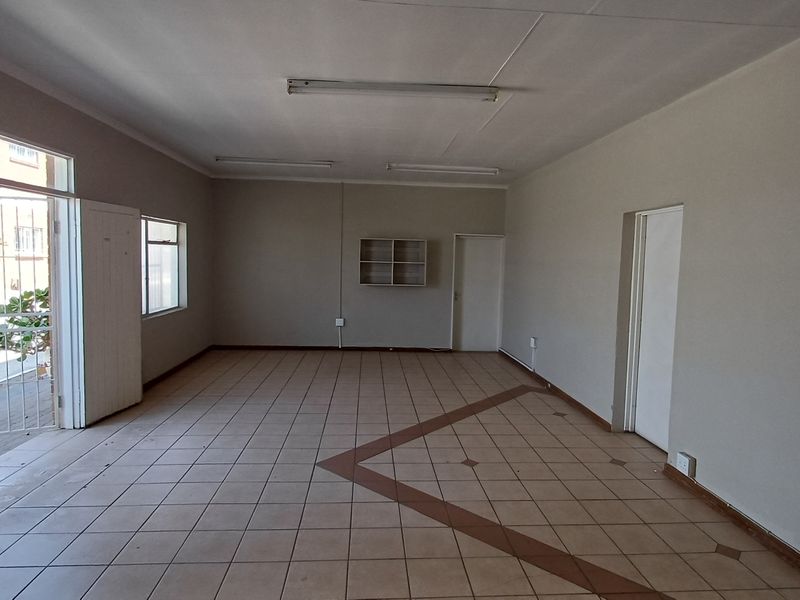 An empty, open-plan office space featuring tiled flooring, fluorescent lighting, and a secure entrance gate, suitable for a variety of professional business uses.