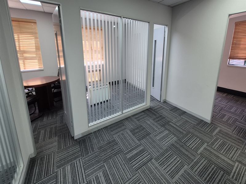 Modern office space featuring glass partitions, patterned carpet tiles, and suspended ceilings, providing a professional and functional work environment.