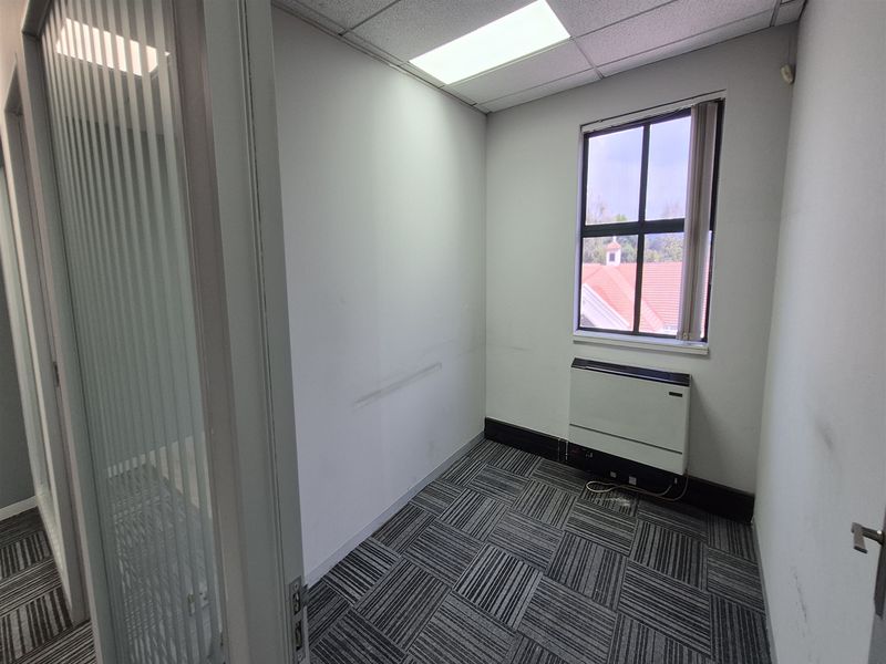 A vacant office space featuring carpet tiles, a glass partition door, recessed lighting, and a wall-mounted heater.