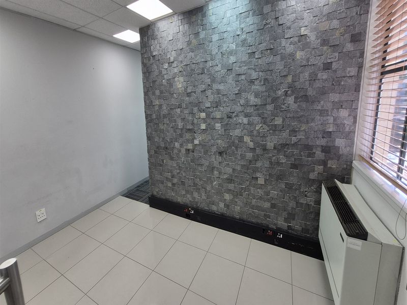 An empty office space featuring a modern stone feature wall, tiled flooring, recessed ceiling lights, and a built-in HVAC unit.