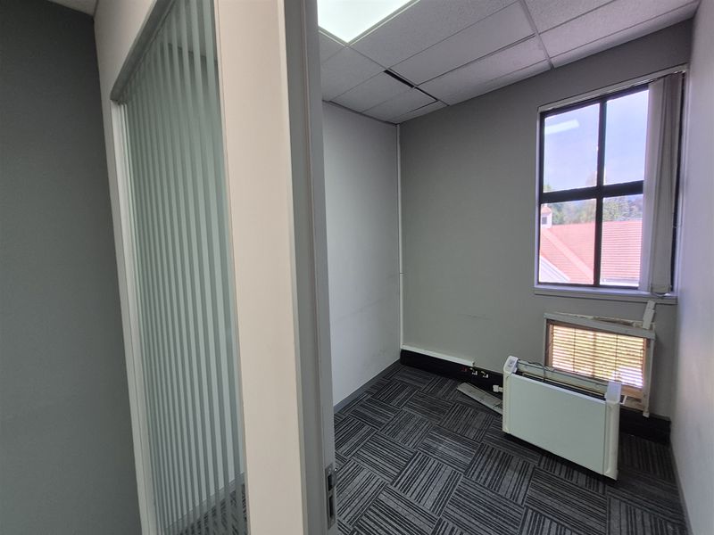 A vacant office space featuring carpet tiles, a suspended ceiling, and a frosted glass partition, offering a functional layout for professional use.
