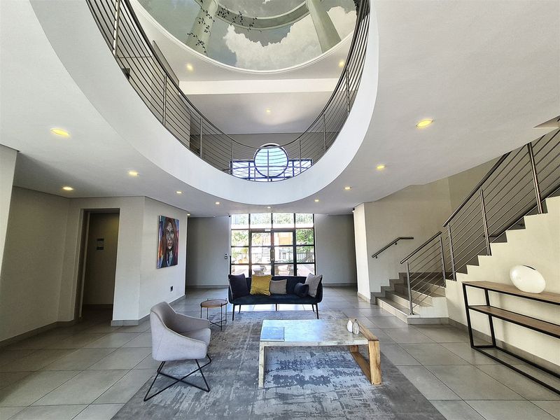 Spacious office building entrance featuring a grand atrium, circular skylight, modern stainless steel balustrades, and tiled flooring.