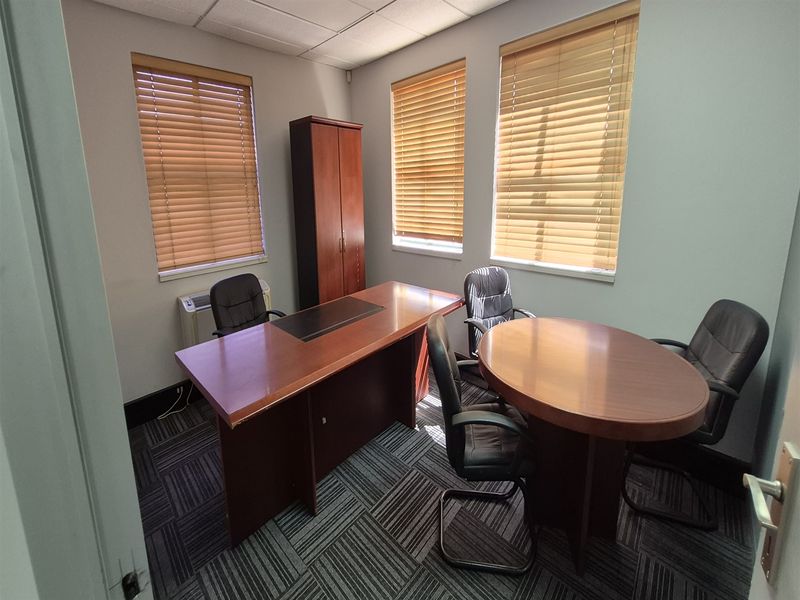 A functional office space featuring carpet tiles, suspended ceiling, and multiple windows with fitted venetian blinds, providing a professional work environment.