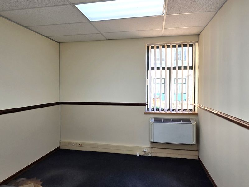 A vacant office space featuring a suspended ceiling, recessed lighting, vertical blinds, and a wall-mounted HVAC unit.