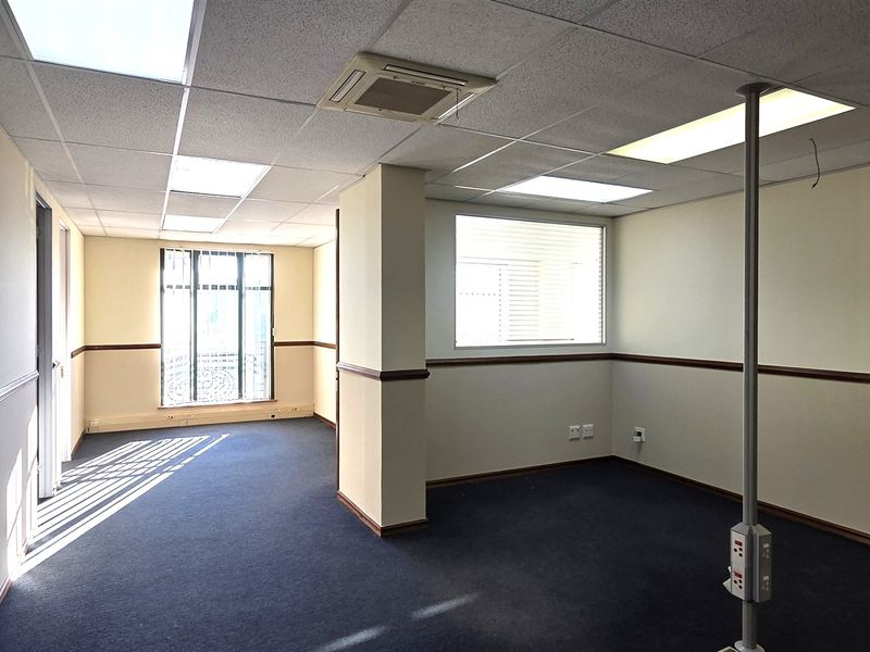 An empty office space featuring a suspended ceiling, recessed lighting, central air conditioning, and carpeted flooring with a central power pole.