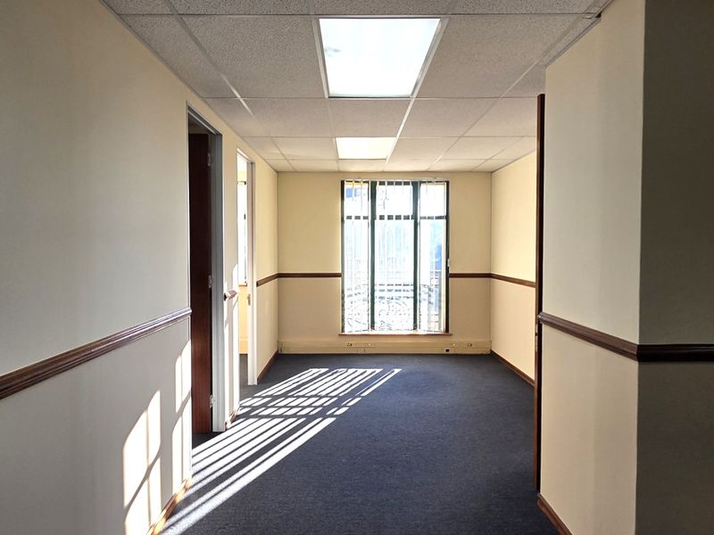 An empty office space featuring a suspended ceiling, recessed lighting, carpeted flooring, and a glass partition, offering a clean and functional professional environment.