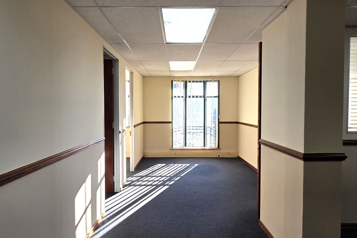 An empty office space featuring a suspended ceiling, recessed lighting, carpeted flooring, and a glass partition, offering a clean and functional professional environment.