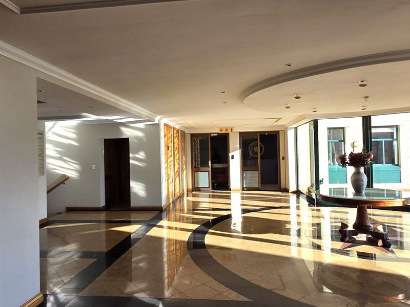 Spacious office building entrance lobby featuring polished marble flooring, recessed ceiling lighting, and large windows providing ample natural light.