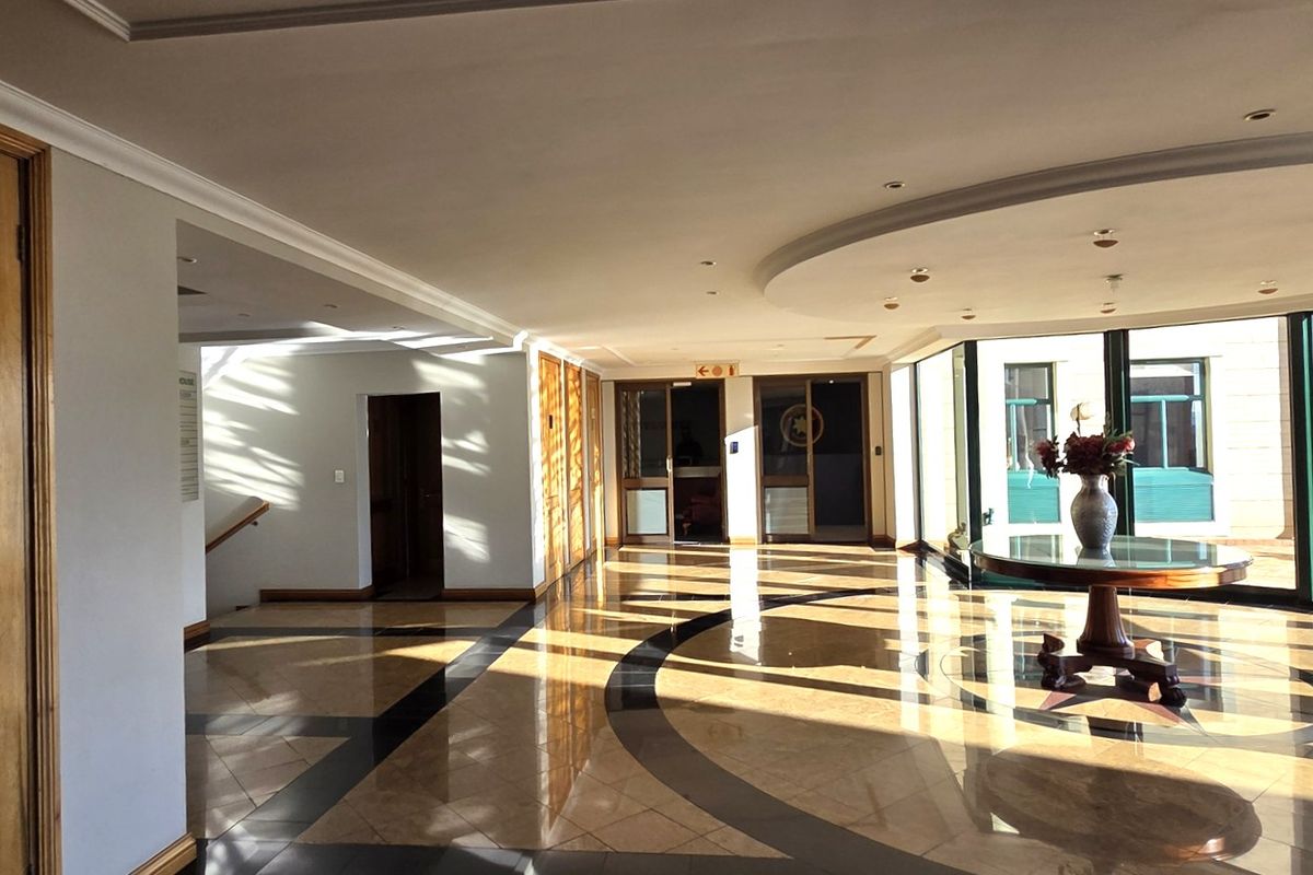 Spacious office building entrance lobby featuring polished marble flooring, recessed ceiling lighting, and large windows providing ample natural light.