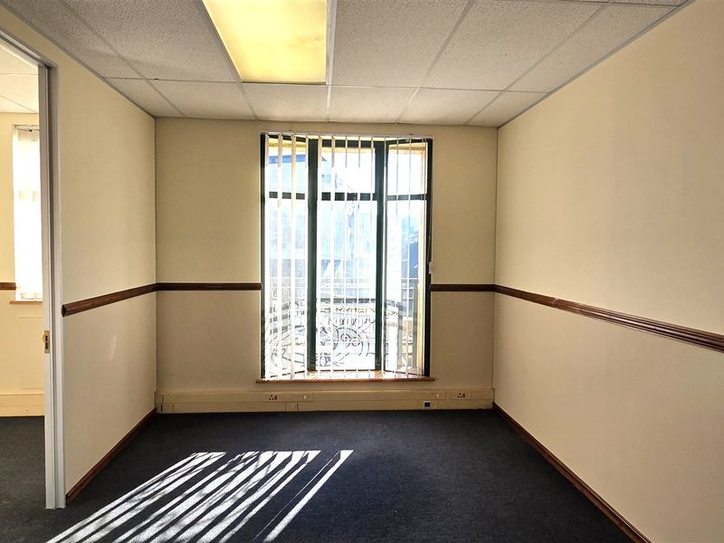 An empty office space featuring a suspended ceiling, recessed lighting, vertical blinds, and carpet flooring with perimeter electrical trunking.