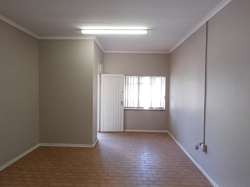 A clean, empty office space featuring neutral walls, tiled flooring, and natural light through a window with vertical blinds.