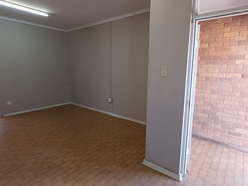 An empty office space featuring neutral walls, tiled flooring, and direct access to an outdoor area with exposed brick finishes.