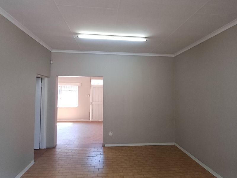A clean, vacant office space featuring neutral wall tones, tiled flooring, and functional overhead lighting, offering a versatile layout for professional use.