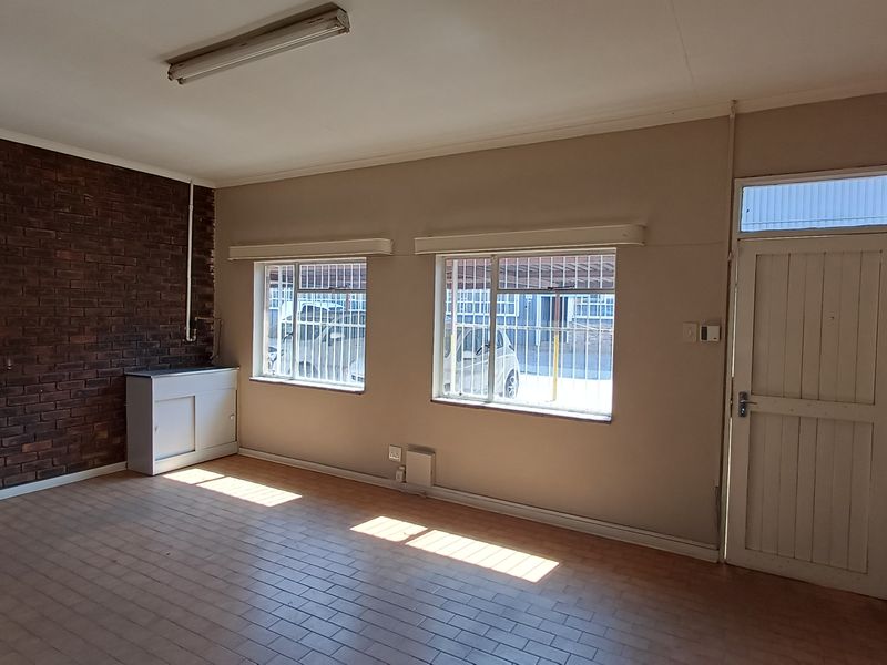 A vacant office space featuring an exposed brick wall, tiled flooring, built-in utility sink, and security bars on the windows.