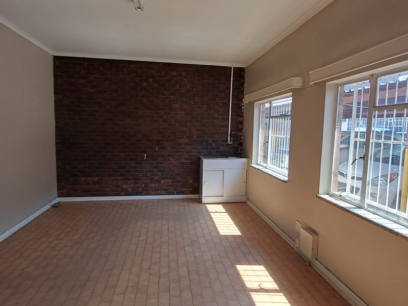 An empty office space featuring an exposed brick wall, tiled flooring, and a built-in sink cabinet with security bars on the windows.