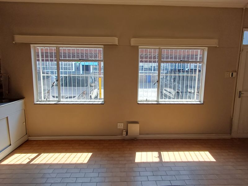 An empty office space featuring a brick accent wall, tiled flooring, security bars on windows, and a built-in sink unit.