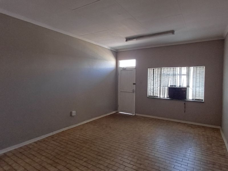 A vacant office space featuring tiled flooring, a built-in air conditioning unit, and window blinds, providing a functional environment for professional use.