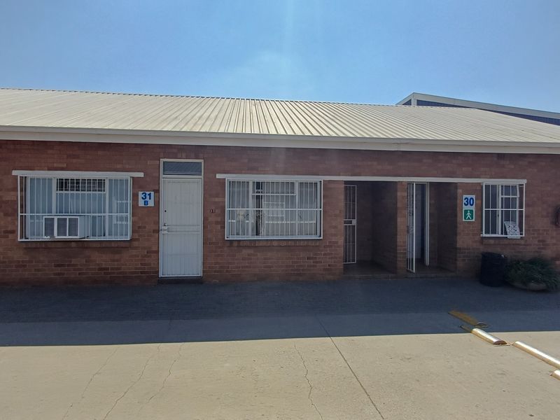 Front elevation of a single-story office building featuring face brick construction, corrugated metal roofing, and secure window and door access points.