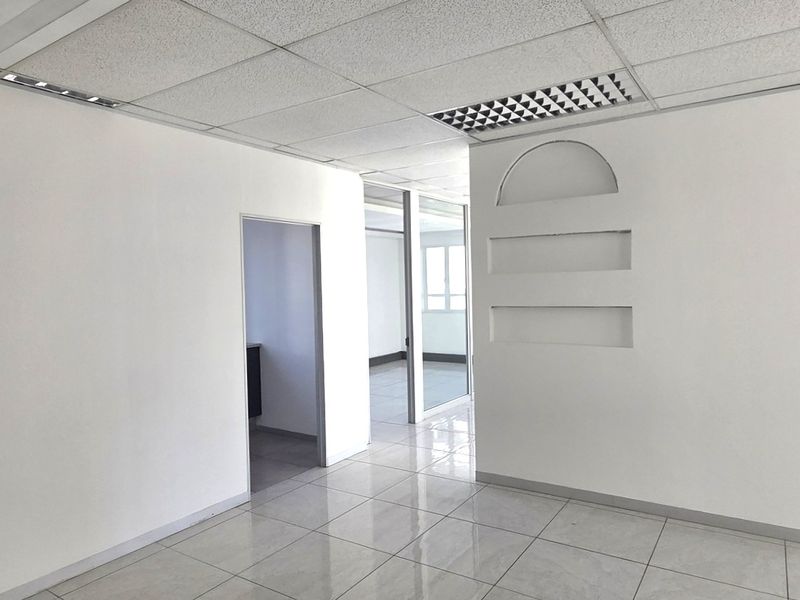 A bright, vacant office space featuring ceramic tile flooring, a suspended ceiling with recessed lighting, and decorative built-in wall niches.