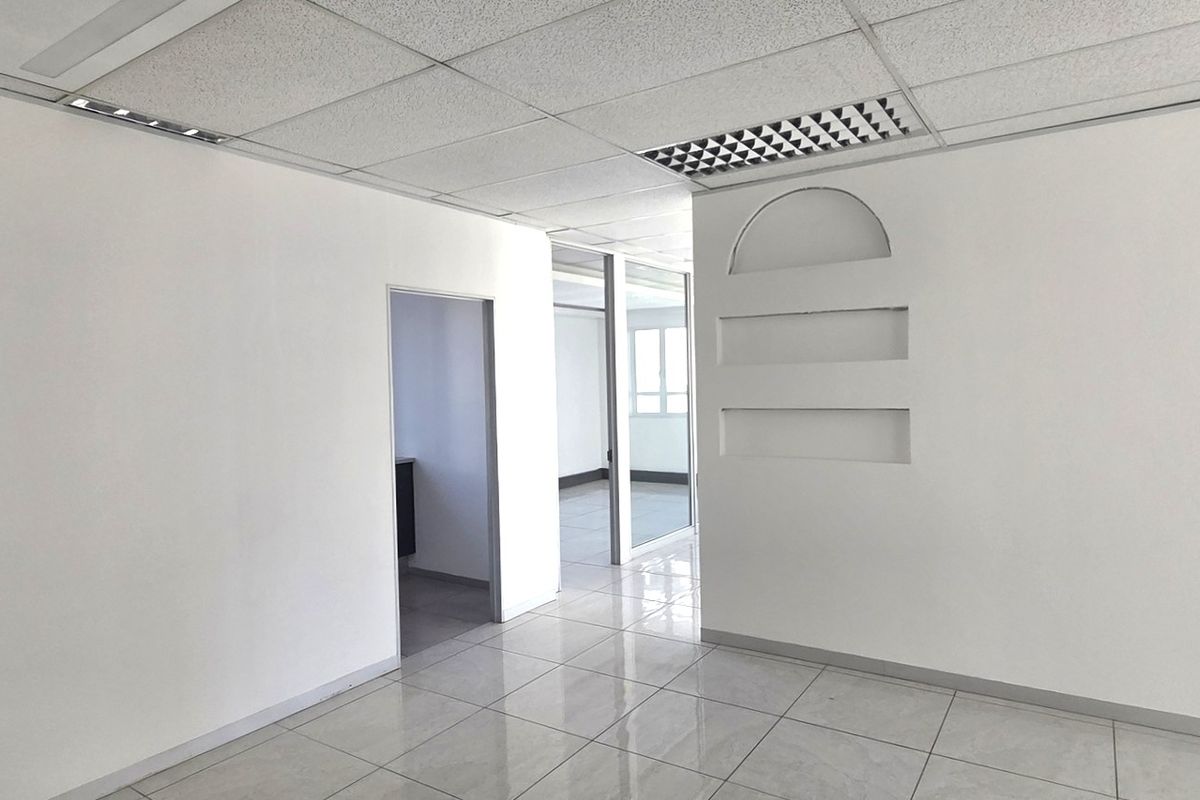 A bright, vacant office space featuring ceramic tile flooring, a suspended ceiling with recessed lighting, and decorative built-in wall niches.