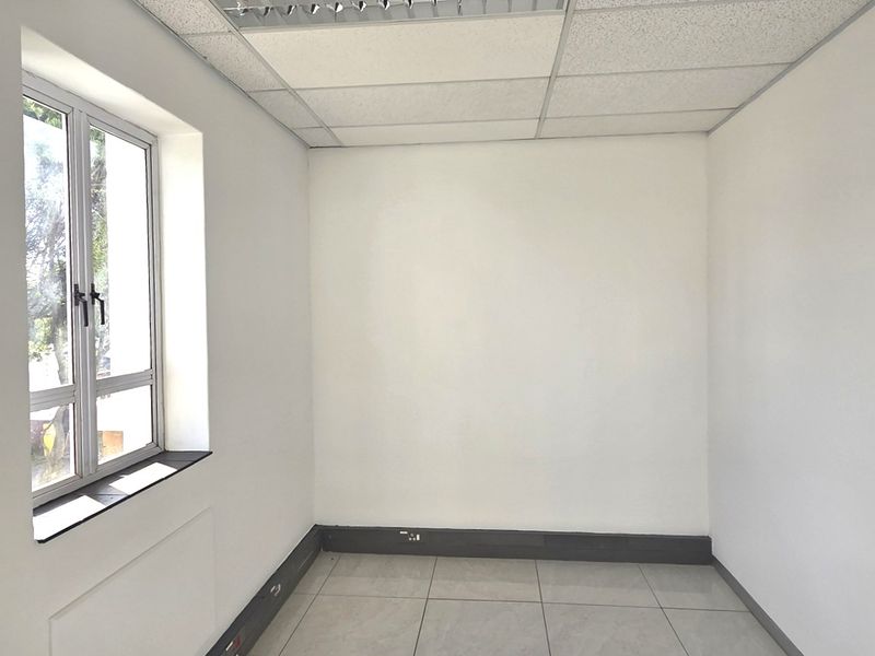 A clean, empty office space featuring a suspended ceiling, tiled flooring, and a window providing natural light.