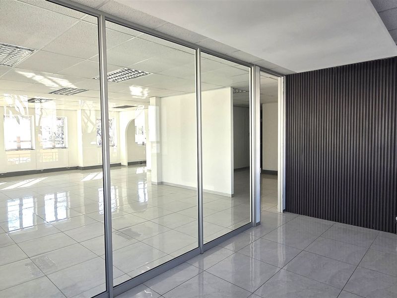 Modern open-plan office space featuring glass partitions, sleek tiled flooring, and a contemporary slatted feature wall, offering a bright and professional work environment.