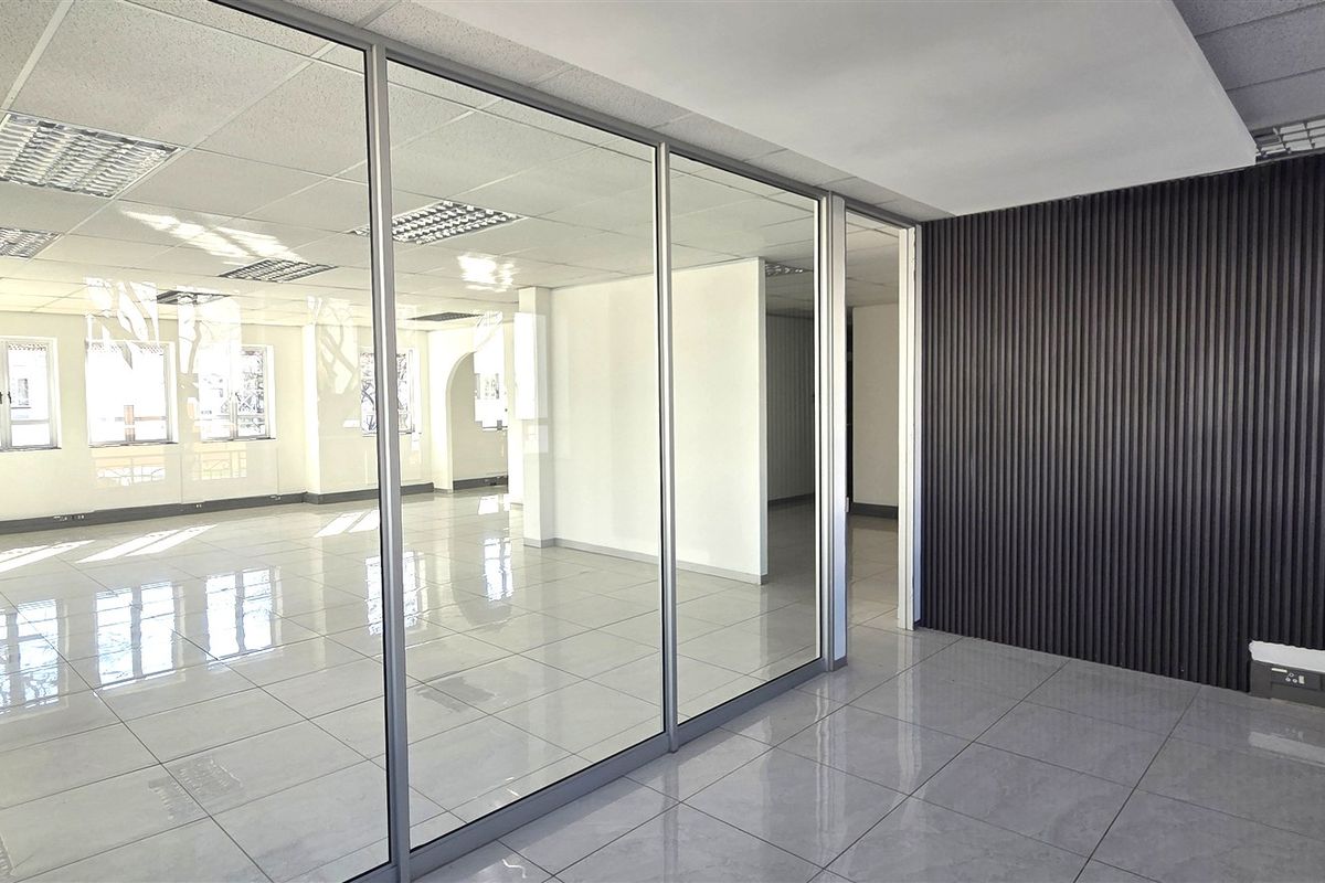 Modern open-plan office space featuring glass partitions, sleek tiled flooring, and a contemporary slatted feature wall, offering a bright and professional work environment.